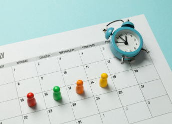 Image of a calendar with four thumbtacks placed on the days Mon-Thurs to represent a four-day work week. There is also a small toy clock on the calendar.